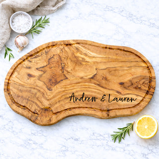 olive wood carving board with personalized family name engraving on a marble surface with kitchen items perfect for wedding, engagement, and housewarming gift