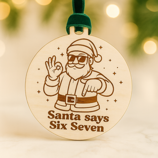 Wooden ornament with a design of Santa Claus and text 'Santa says Six Seven' against a blurred Christmas tree background.