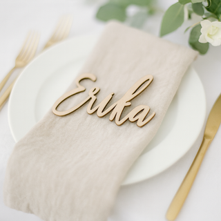 Wooden name card with 'Erika' on a beige napkin over a white plate with gold cutlery.
